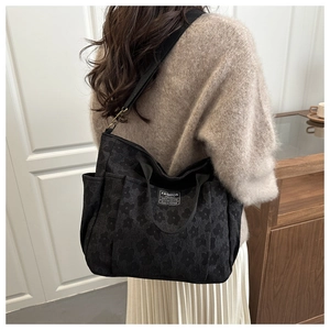 Detail of black floral jacquard canvas tote bag featuring an embroidered fashion logo tag