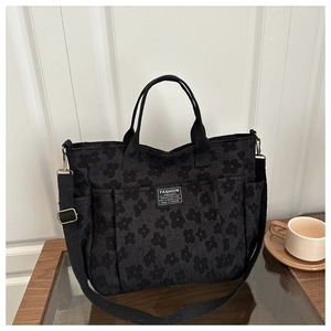 Detail of black floral tote bag featuring functional front pockets and adjustable strap