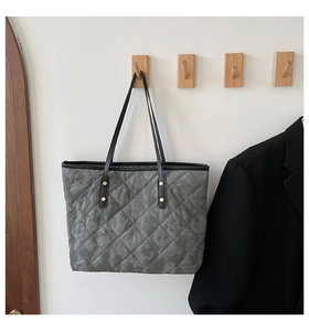 Detail of grey quilted tote bag with diamond stitching, dark camo pattern and gold rivets