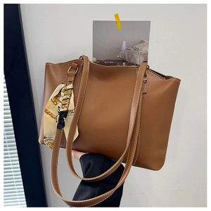 Detail of a brown tote bag featuring white contrast stitching and a floral silk scarf