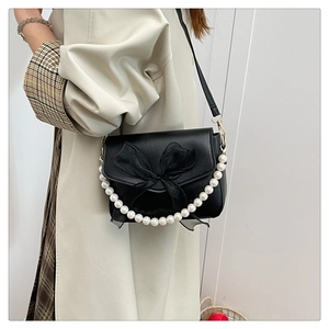 Detail of black crossbody bag featuring a silk bow and pearl handle chain for women