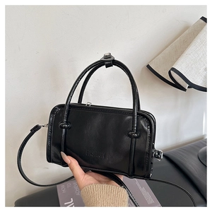 Detail of a black glossy patent leather handbag featuring embossed fashion lettering