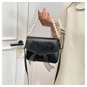 Detail of a black handbag with an organza bow, pearl handle, and golden hardware