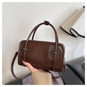 Detail of dark brown glossy rectangular handbag with FASHION embossing and round handles