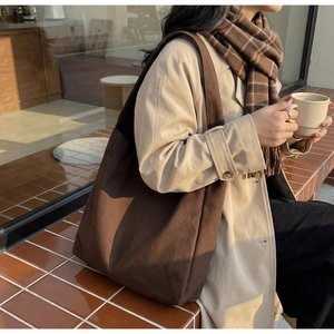 Detail of a large brown canvas tote bag on a model in a cozy outdoor autumn setting
