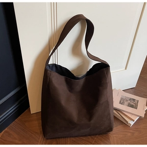 Dettaglio della borsa hobo in pelle scamosciata marrone scuro davanti a una porta bianca