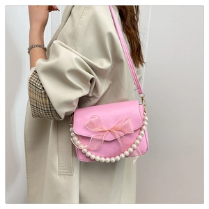 Detail of pink crossbody bag with organza bow and large pearl chain on beige coat