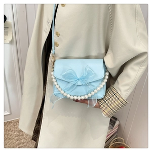 Detail of light blue handbag featuring a decorative mesh bow and white pearl handle strap