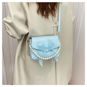 Close-up of sky blue crossbody bag with mesh bow and pearl handle on a beige coat