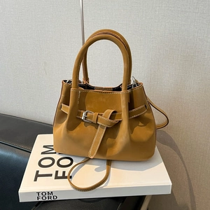 Minimalist camel crossbody bag with belt detail and top handle on a white book