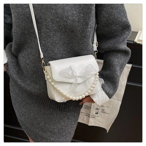 Detail of white crossbody bag with sheer bow and pearl chain on a grey knit outfit