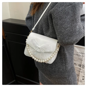 White commute bag with pearl handle and tulle bow shown on shoulder in minimalist setting