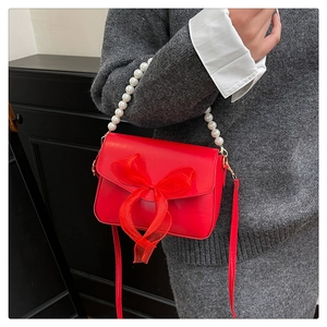 Detail of red leather bag featuring a large organza bow and white pearl beaded handle