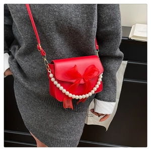 Detail of red crossbody bag with mesh bow, pearl handle on grey knit dress