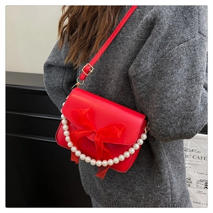 Detail of red leather crossbody bag featuring a large mesh bow and white pearl chain