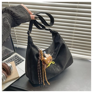 Detailed view of black hobo shoulder bag with a brown teddy bear charm on office desk