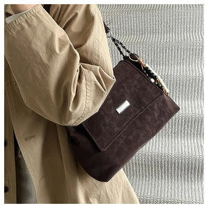 Detail of dark brown suede shoulder bag with beaded metal chain strap and silver buckle