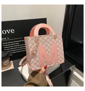 Detail view of pink leather tote bag with M letter monogram print and gold hardware