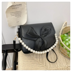 Detail of black leather handbag featuring a silk bow decoration and large pearl handle strap