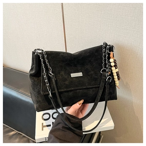 Detail of a vintage black leather shoulder bag with a silver chain and beaded charm
