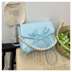 Detail of light blue crossbody bag with a large tulle bow and elegant pearl handle
