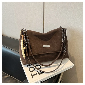 Detail of vintage brown suede bag with metal chain strap and wooden bead pendant