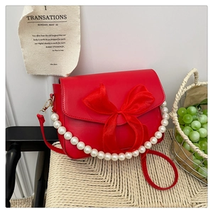 Detail of red crossbody bag with oversized bow and elegant pearl chain trim