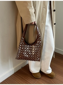 Detail of a brown studded hobo bag styled with a trench coat for a modern fashion look