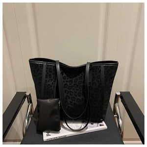 Détail d'un sac cabas noir imprimé léopard sur fauteuil en cuir avec petite pochette