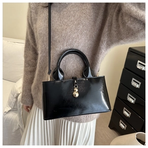 Dettaglio di una borsa in vernice nera con ciondolo a sfera dorata su un maglione beige
