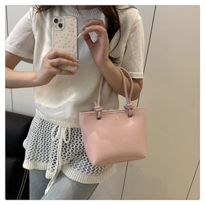 Detail of light pink glossy leather handbag featuring unique knot handles and metal rings