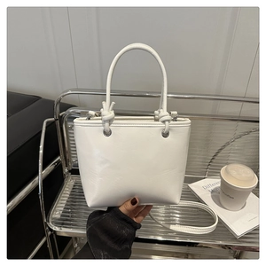 Close-up of white leather bucket bag featuring a decorative knot handle and metal rings