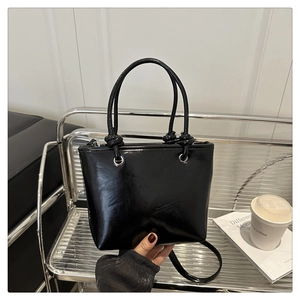 Close-up of black glossy leather tote bag showing knot detail and silver metal hardware