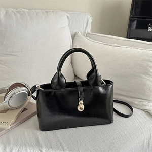 Elegante borsa a mano da donna in pelle verniciata nera con ciondolo a sfera dorato