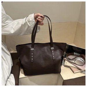 Detail of dark brown leather tote bag with silver star rivets and metal bar accents