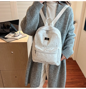 Detailed view of white leather backpack with silver star pattern and front zipper pocket