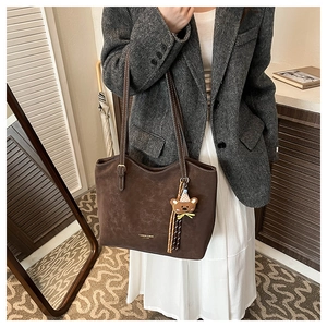 Detail of brown suede tote bag with golden logo lettering and a cute bear bag charm