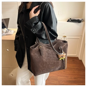 Detailed shot of brown matte leather tote bag featuring a teddy bear charm and gold logo