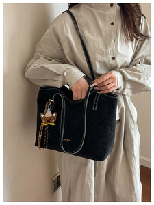 Detail of black suede tote bag with white contrast stitching and a cute bear charm