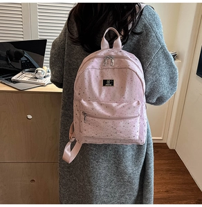 Close-up of pink backpack with silver star patterns worn by a model in a home setting