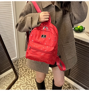 Detail of red backpack with star pattern featuring front zipper and metal logo
