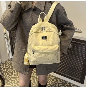 Detail of light yellow backpack with silver star patterns and brand logo on canvas
