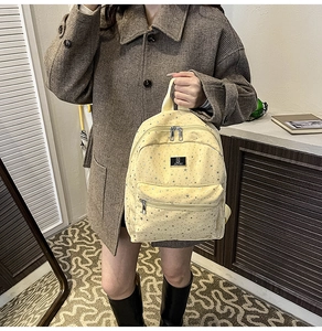 Detail of light yellow star-print backpack with front zipper pocket and logo