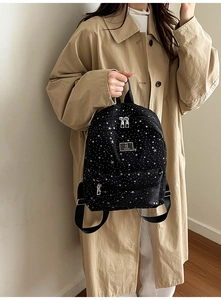 Detail of black backpack with white star patterns and front zip pocket held by a model