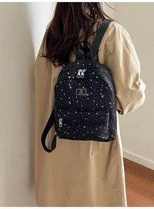 Rear view of a black backpack with white star patterns and adjustable straps on model
