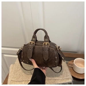 Close-up of deep brown Boston bag with gold buckles and dual handles in a lifestyle setting