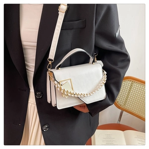 Dettaglio borsa a tracolla in pelle bianca con chiusura dorata su completo blazer nero