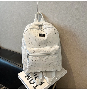 Detail of white star print backpack showing metal logo plaque and front zipper pocket