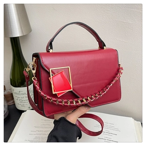 Dettaglio borsa bordeaux in pelle opaca con fibbia dorata e tracolla a catena intrecciata