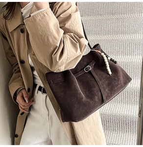 Dettaglio della borsa tote in pelle scamosciata marrone con fibbia e ciondolo di perle